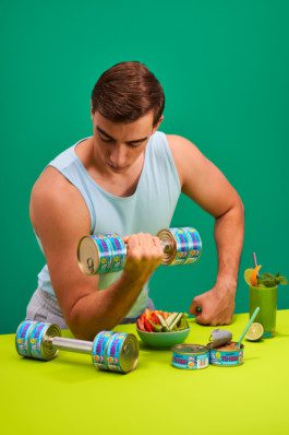 Ein Mann trainiert mit Hanteln aus Dosen von BettaF!sh sitzend an einem Tisch fotografiert von Werbefotografen Silly berlin. 